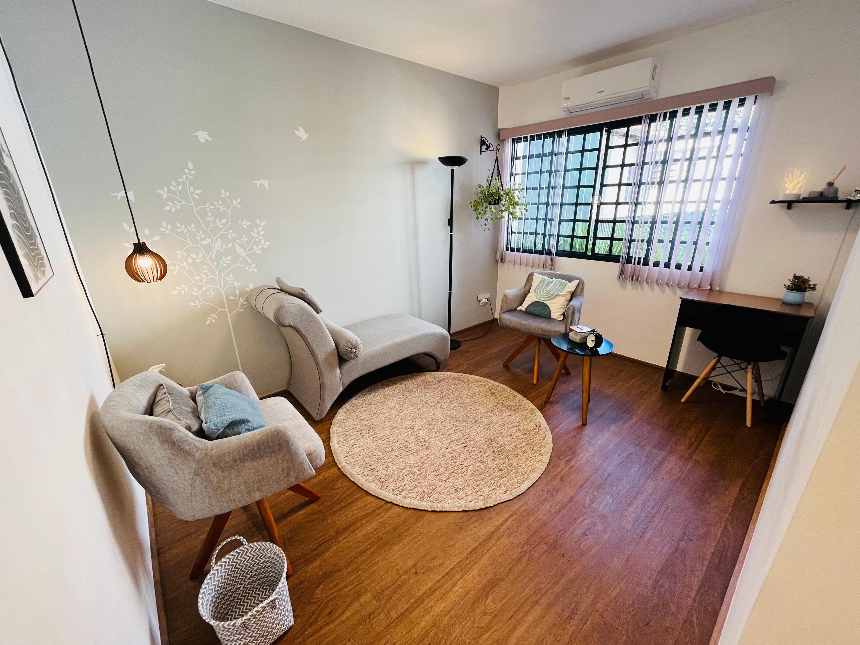 Sala 6 com divã cinza, duas poltronas bege, tapete redondo, luminária pendente e adesivo de árvore na parede