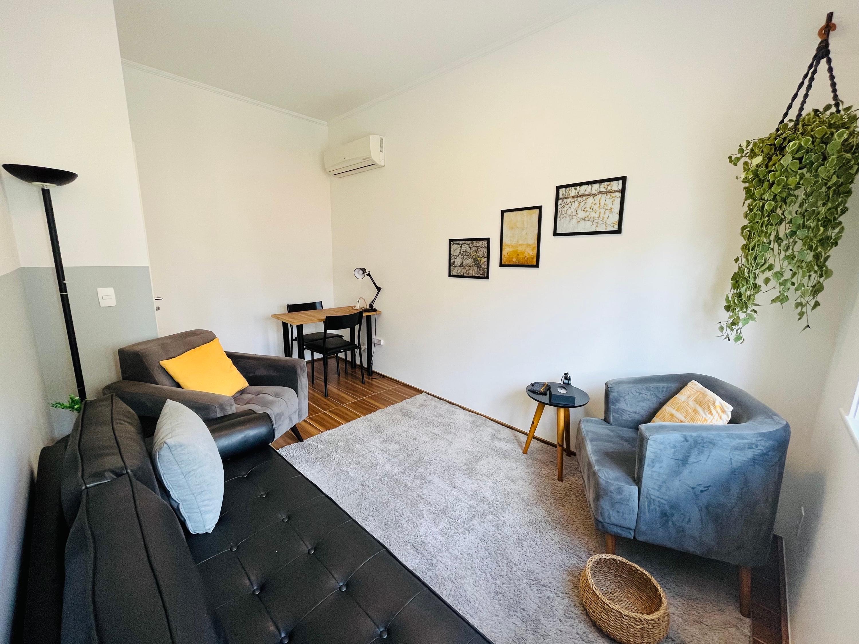 Sala 3 com divã de couro preto, duas poltronas de almofadas amarelas e escrivaninha ao fundo