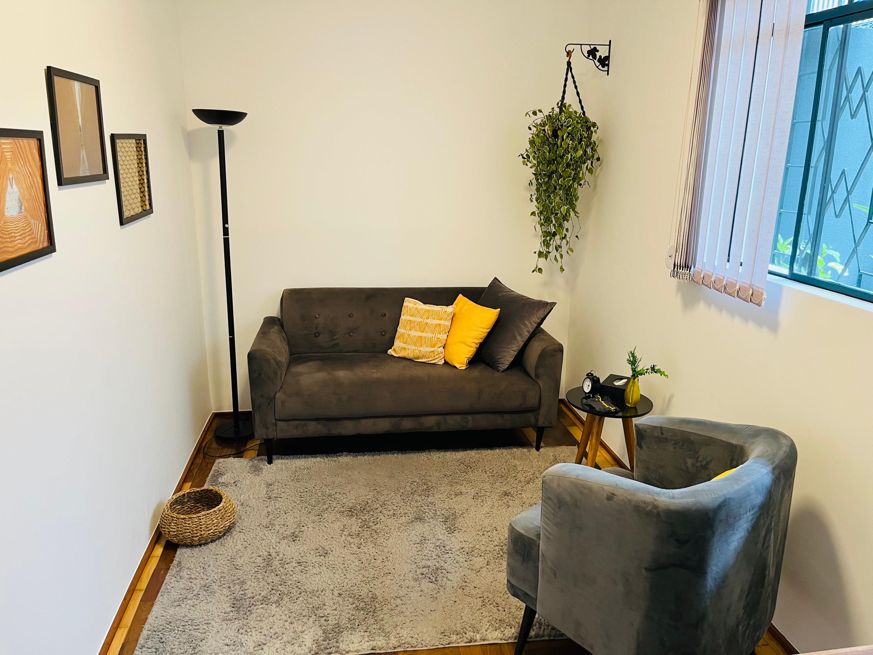 Sala 1 com sofá cinza de almofadas amarelas, poltrona cinza, tapete e quadros na parede
