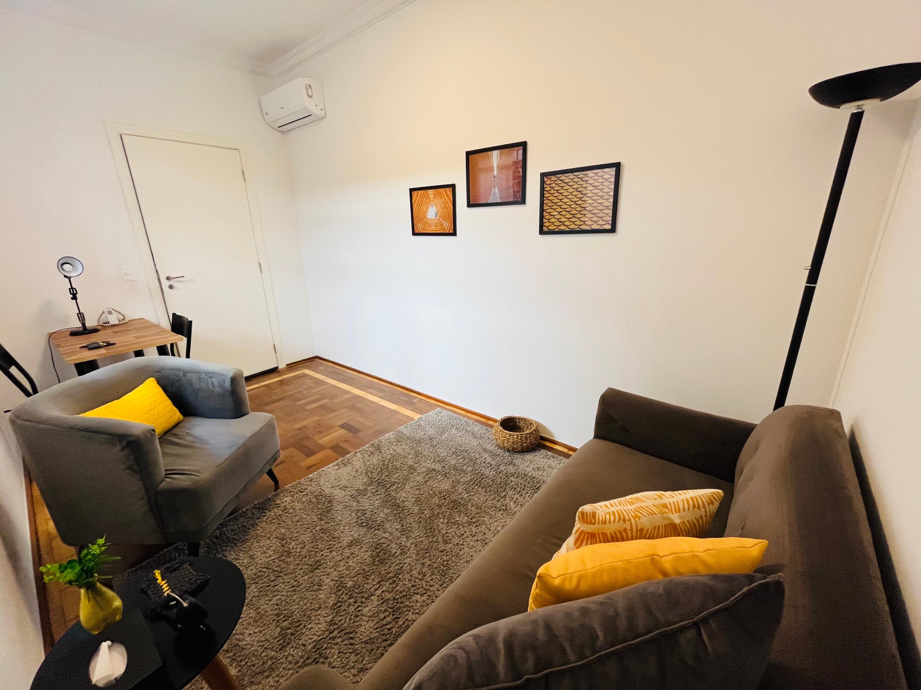 Sala 1 com poltrona cinza, escrivaninha, ar-condicionado e três quadros na parede