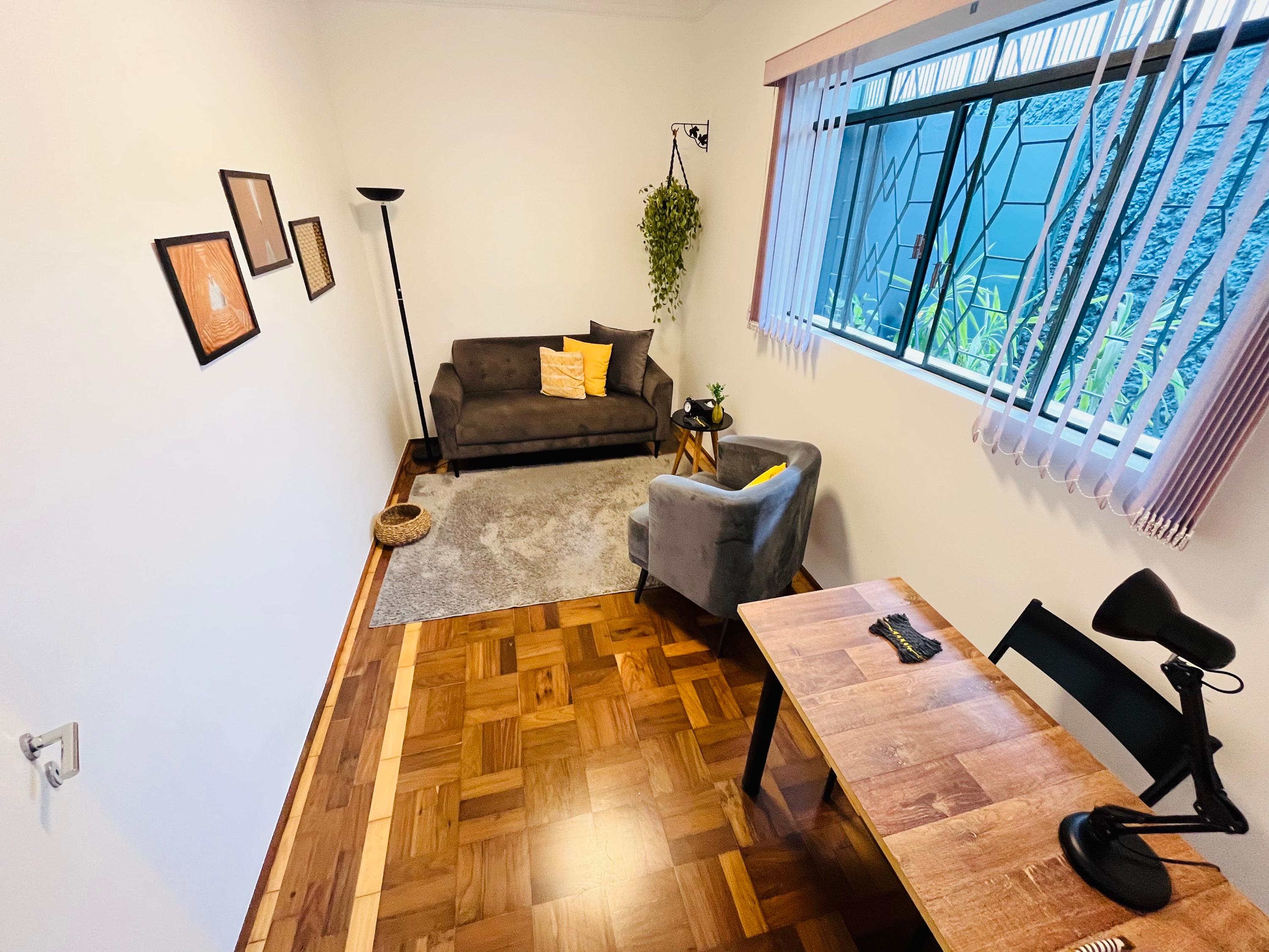 Sala 1 vista da porta, com piso de taco, escrivaninha e sofá ao fundo