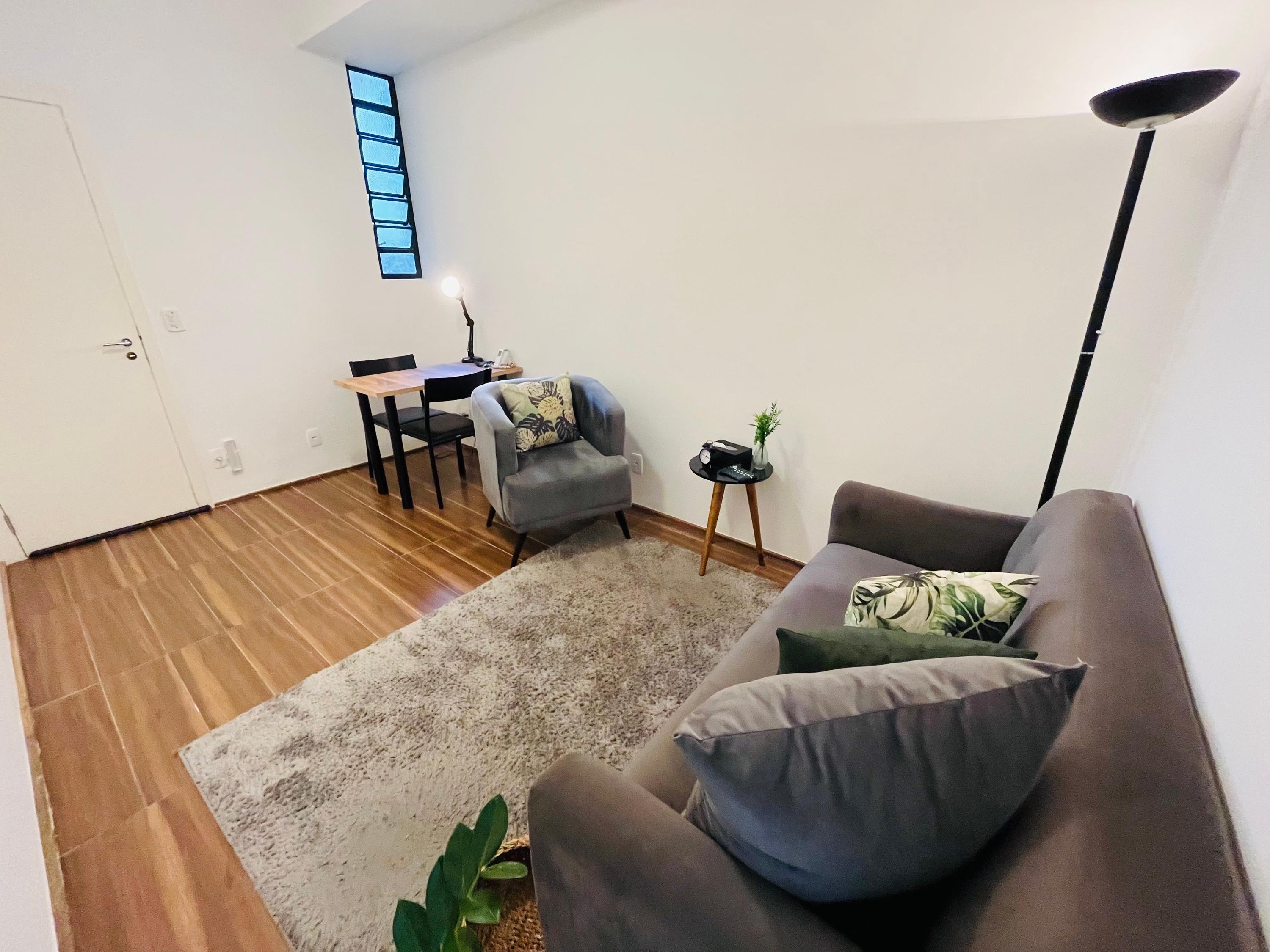 Sala 2 com poltrona, escrivaninha junto à porta e sofá em primeiro plano
