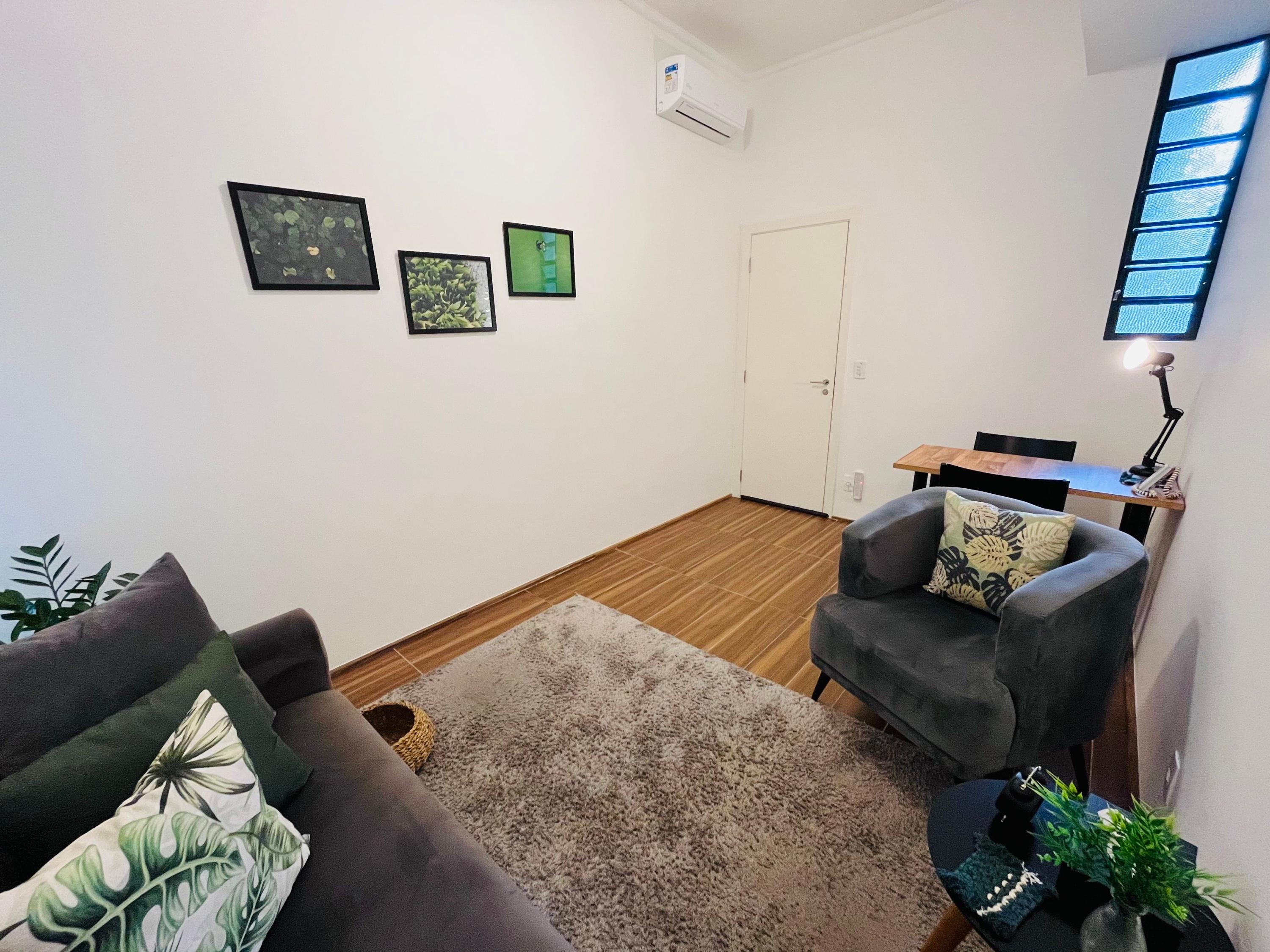 Sala 2 com quadros de folhagens, poltrona cinza e escrivaninha