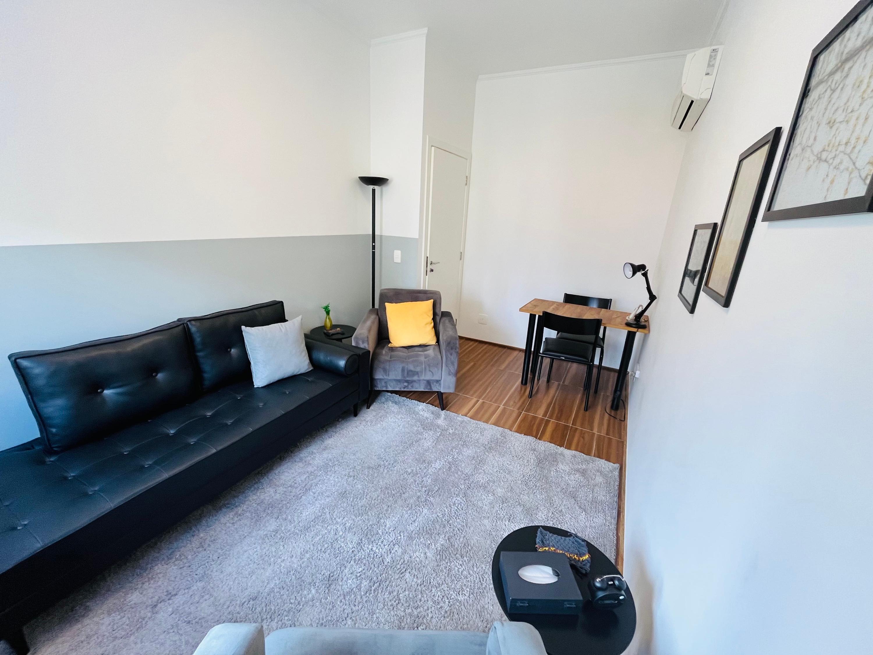 Sala 3 com divã de couro preto, poltrona de almofada amarela e escrivaninha ao fundo