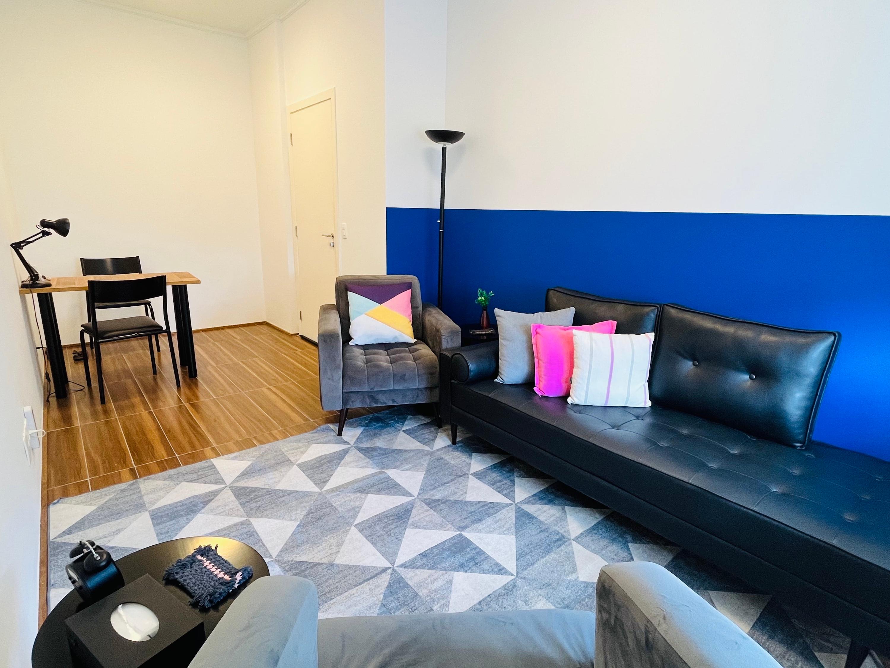 Sala 4 com divã de couro preto junto à parede azul, poltrona e escrivaninha ao fundo