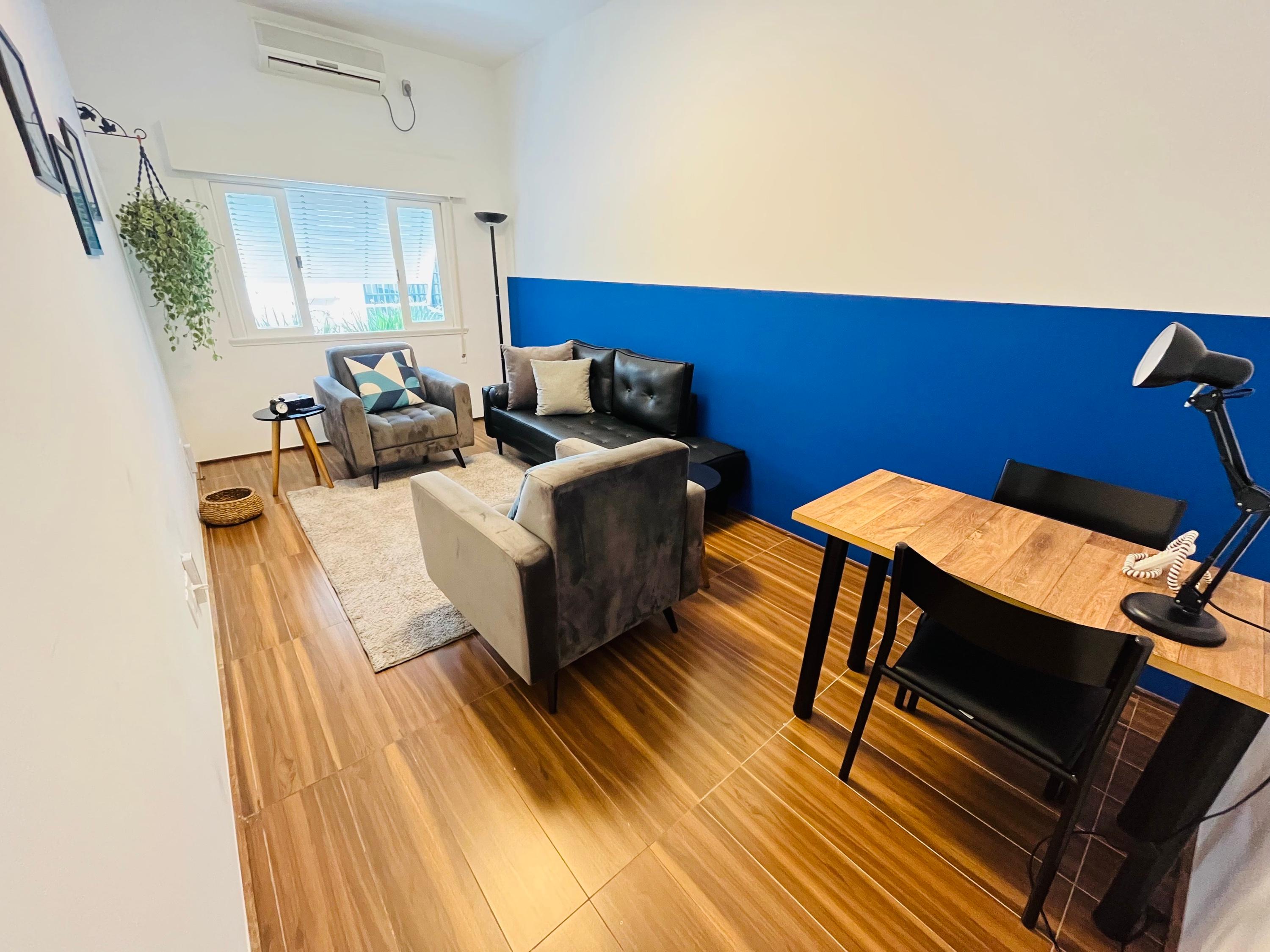 Sala 5 vista da porta, com escrivaninha, poltrona e divã junto à parede azul