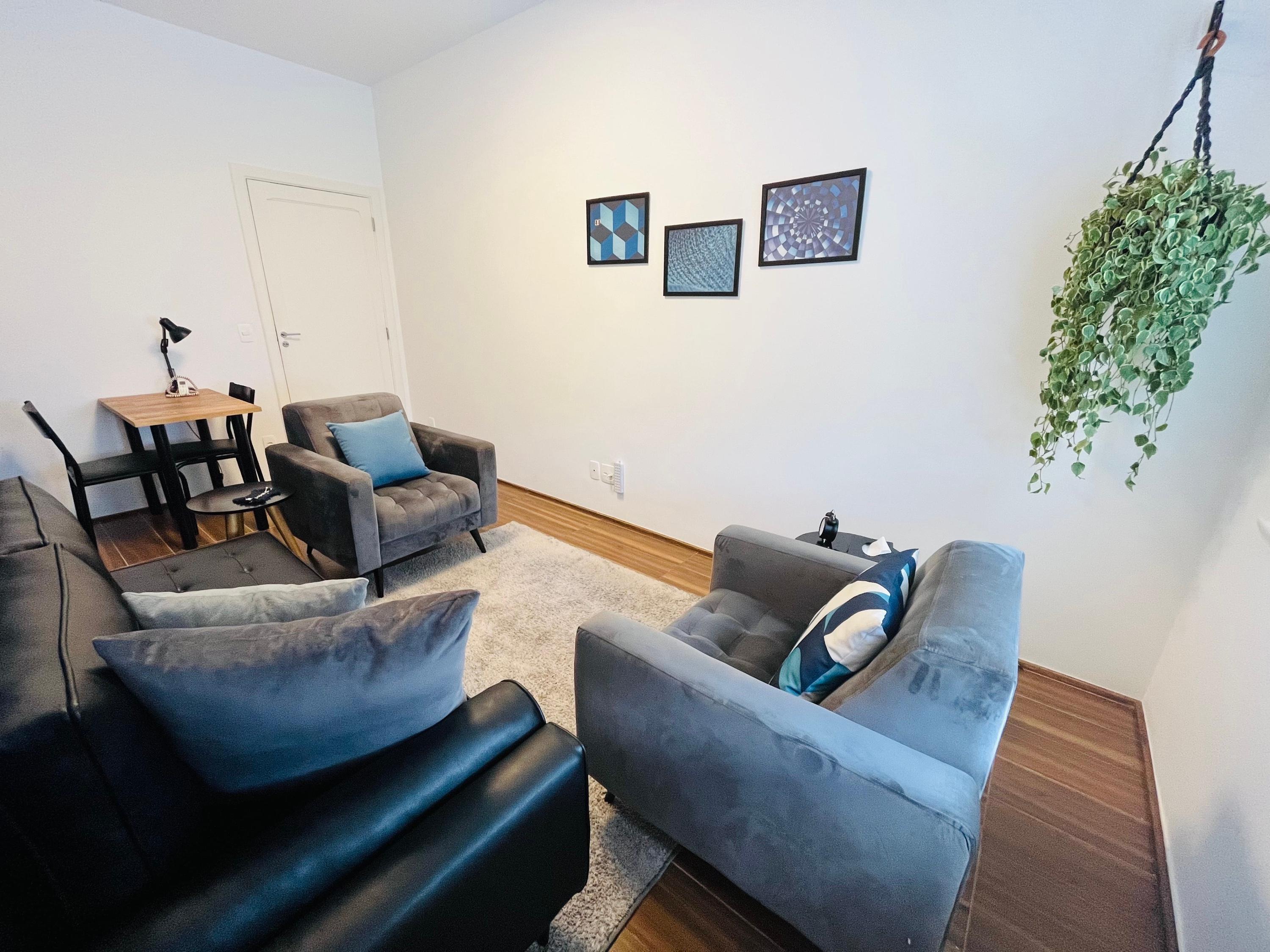 Sala 5 com poltrona cinza, quadros azuis na parede e divã de couro em primeiro plano