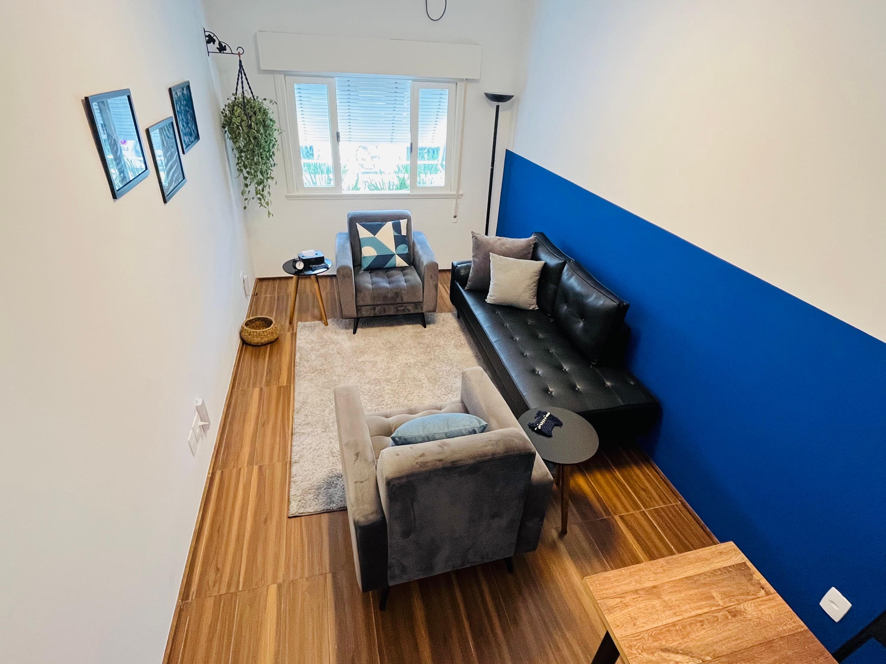 Sala 5 vista de cima, com divã de couro, poltronas e parede azul