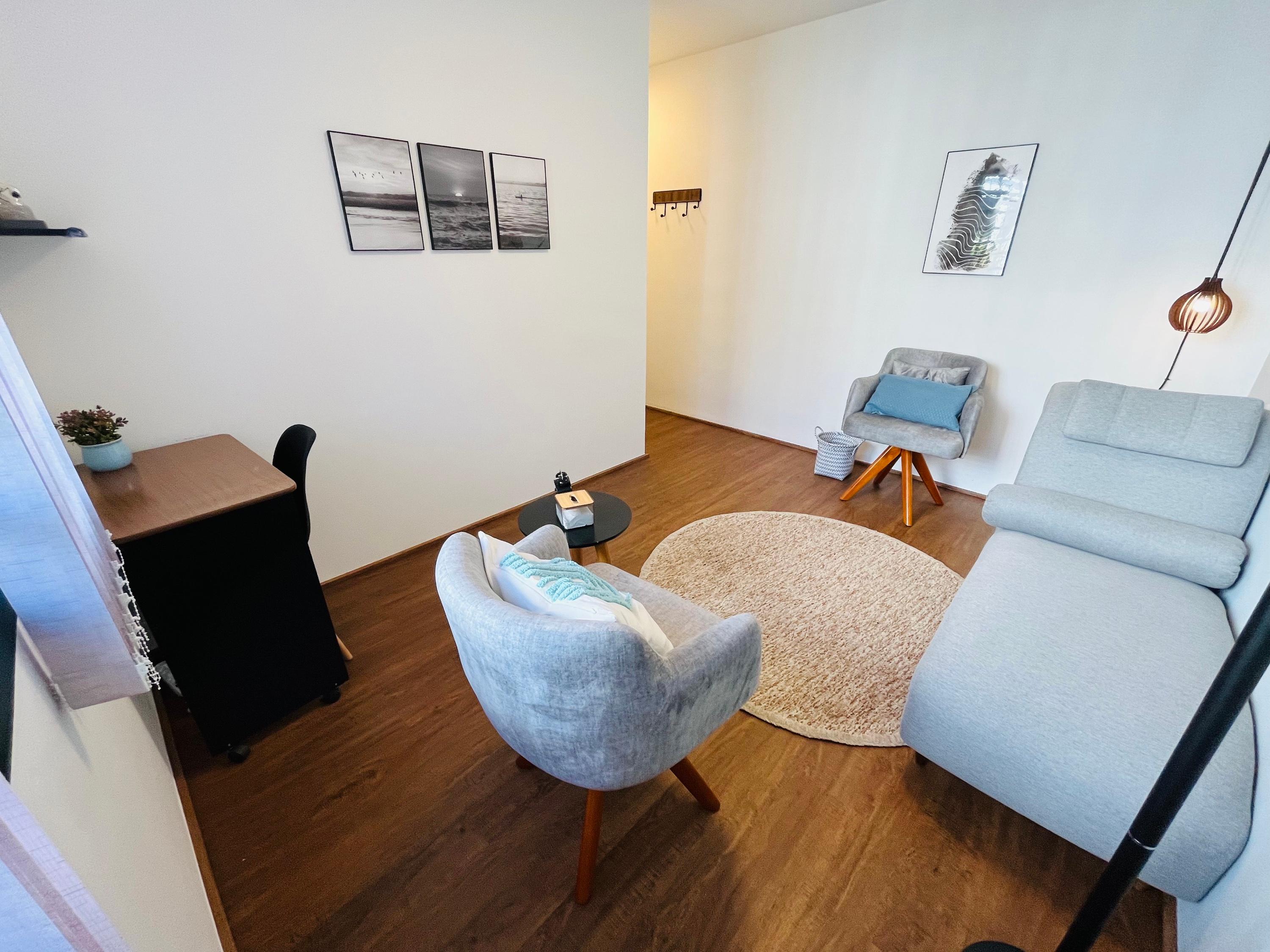 Sala 6 com poltrona, tapete redondo, divã e escrivaninha junto à janela