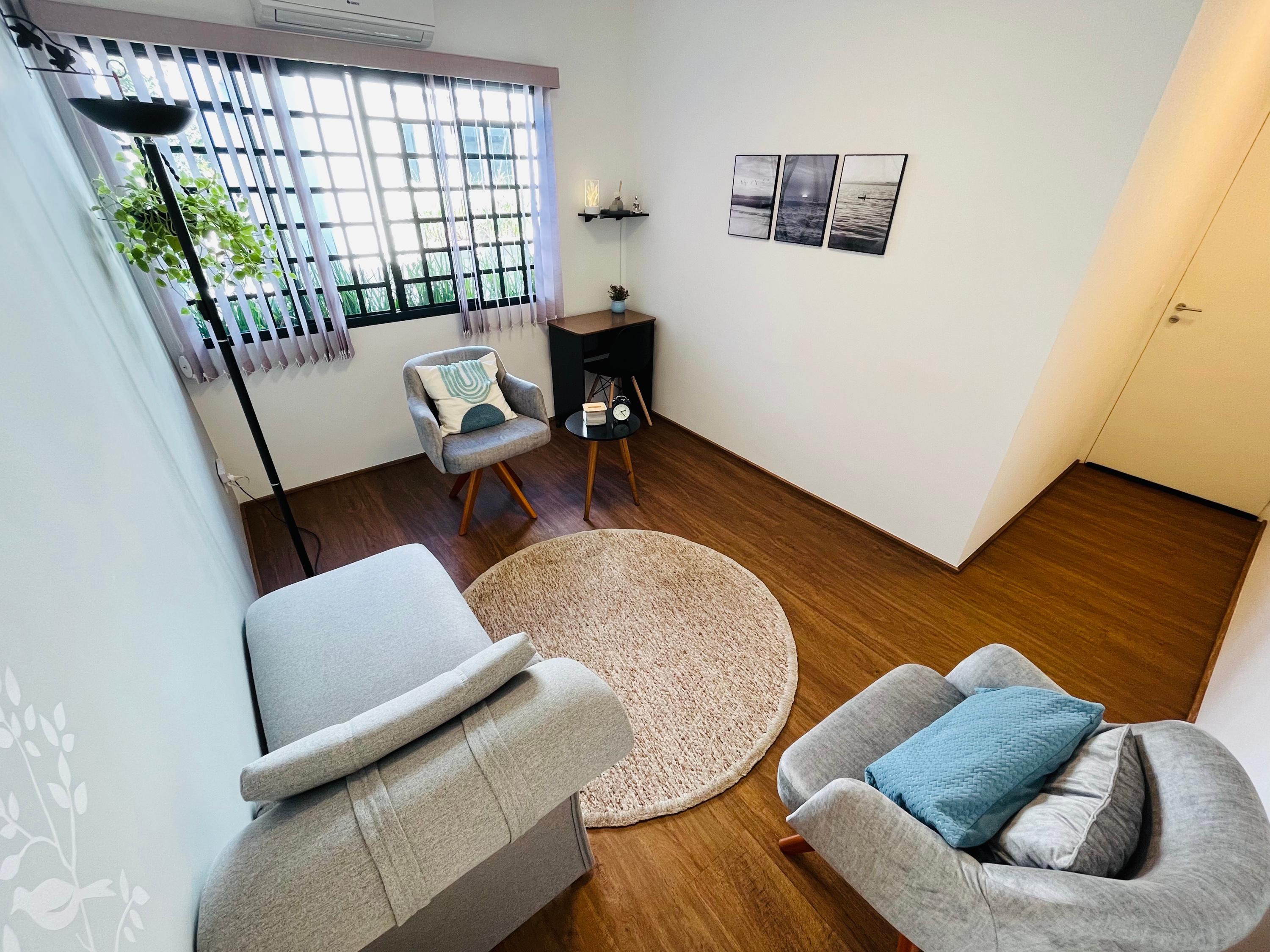 Sala 6 com poltronas, tapete redondo e janela com persiana