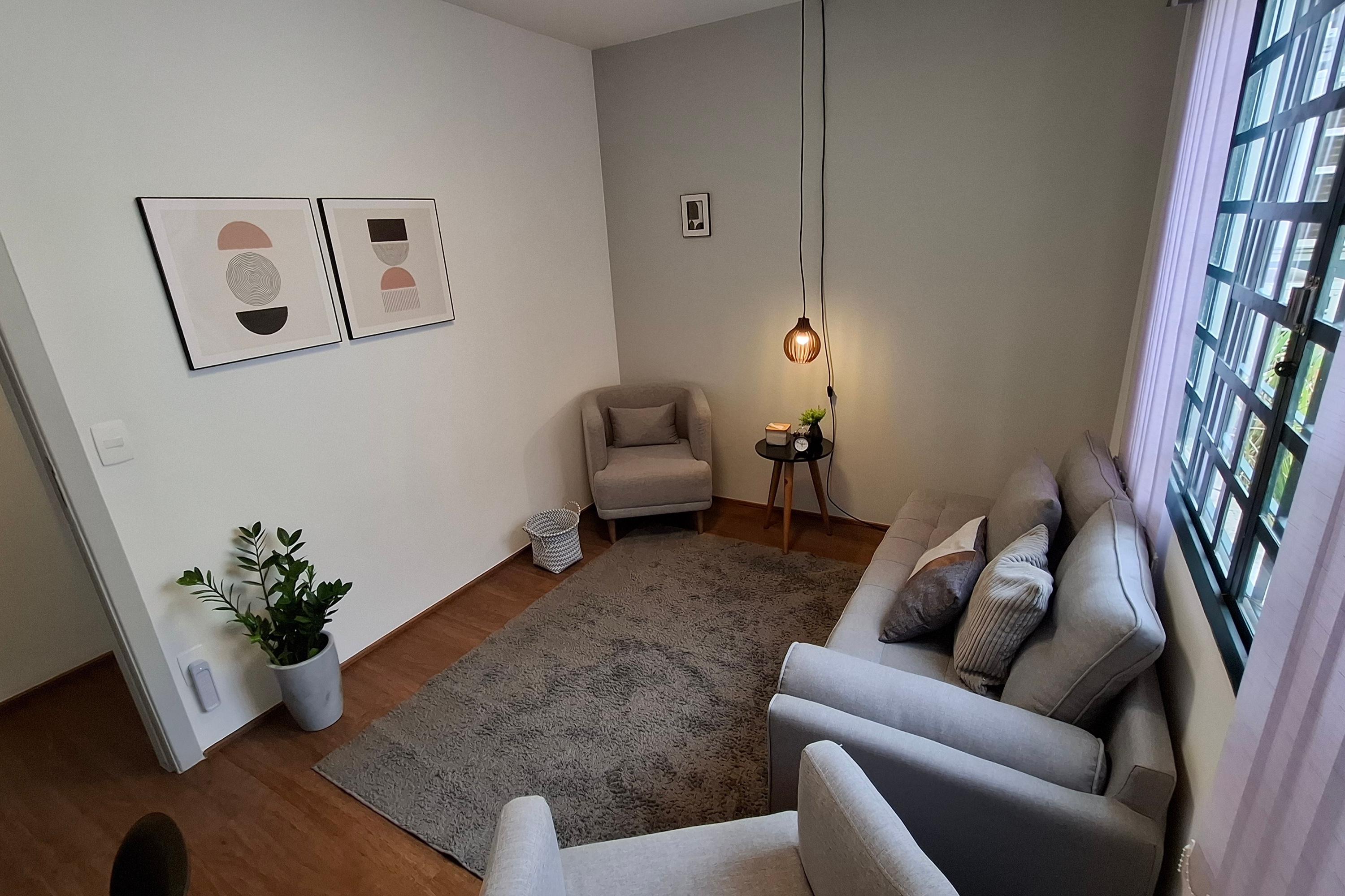 Sala 7 vista da porta, com divã cinza, poltrona bege, luminária pendente e janela