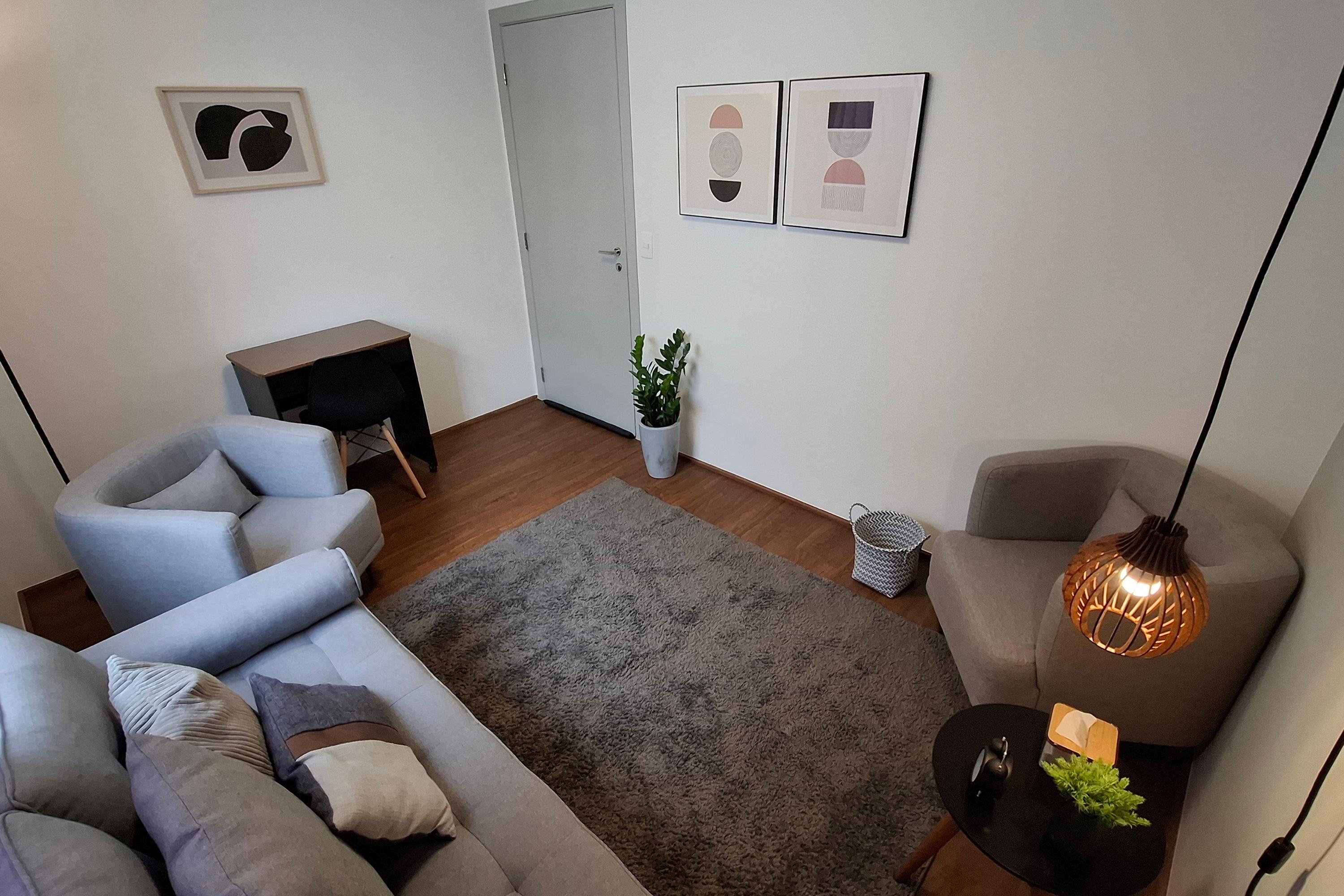 Sala 7 com escrivaninha, divã cinza, poltrona e luminária pendente sobre a mesa de apoio