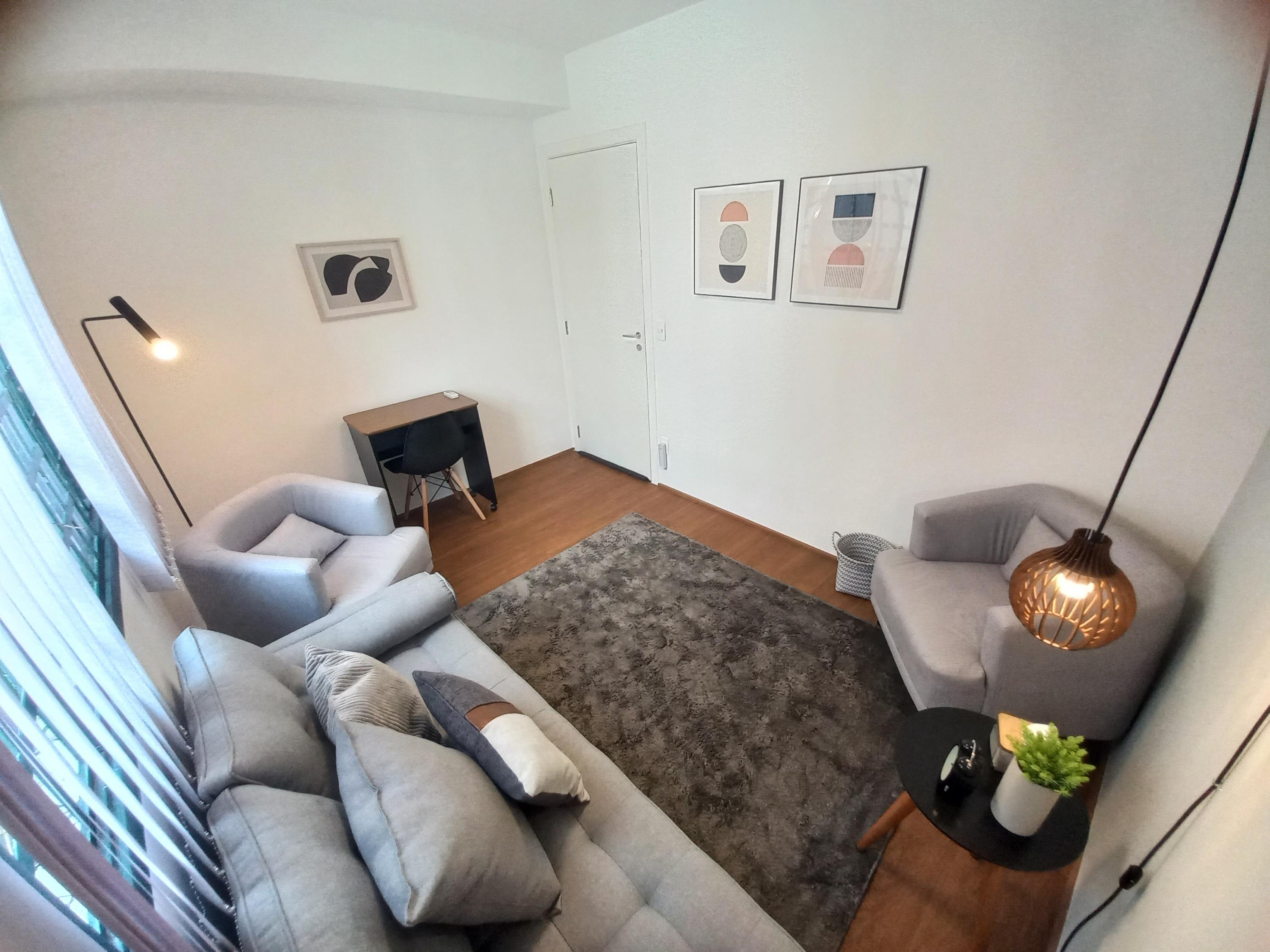 Sala 7 vista da janela, com divã cinza, escrivaninha e quadros na parede